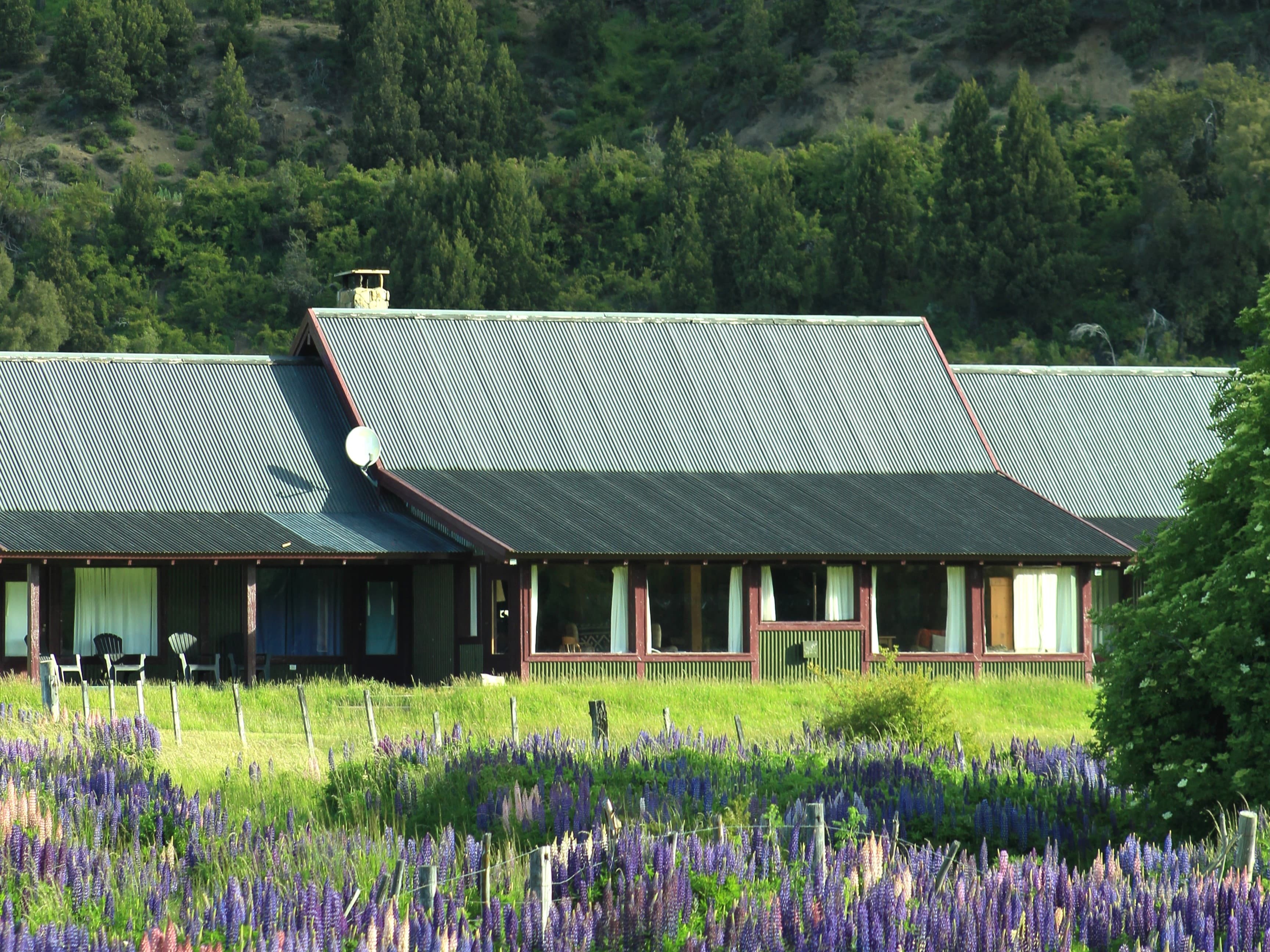 Instalaciones de La Pilarica Lodge junto a tres autos y montañas nevadas de fondo