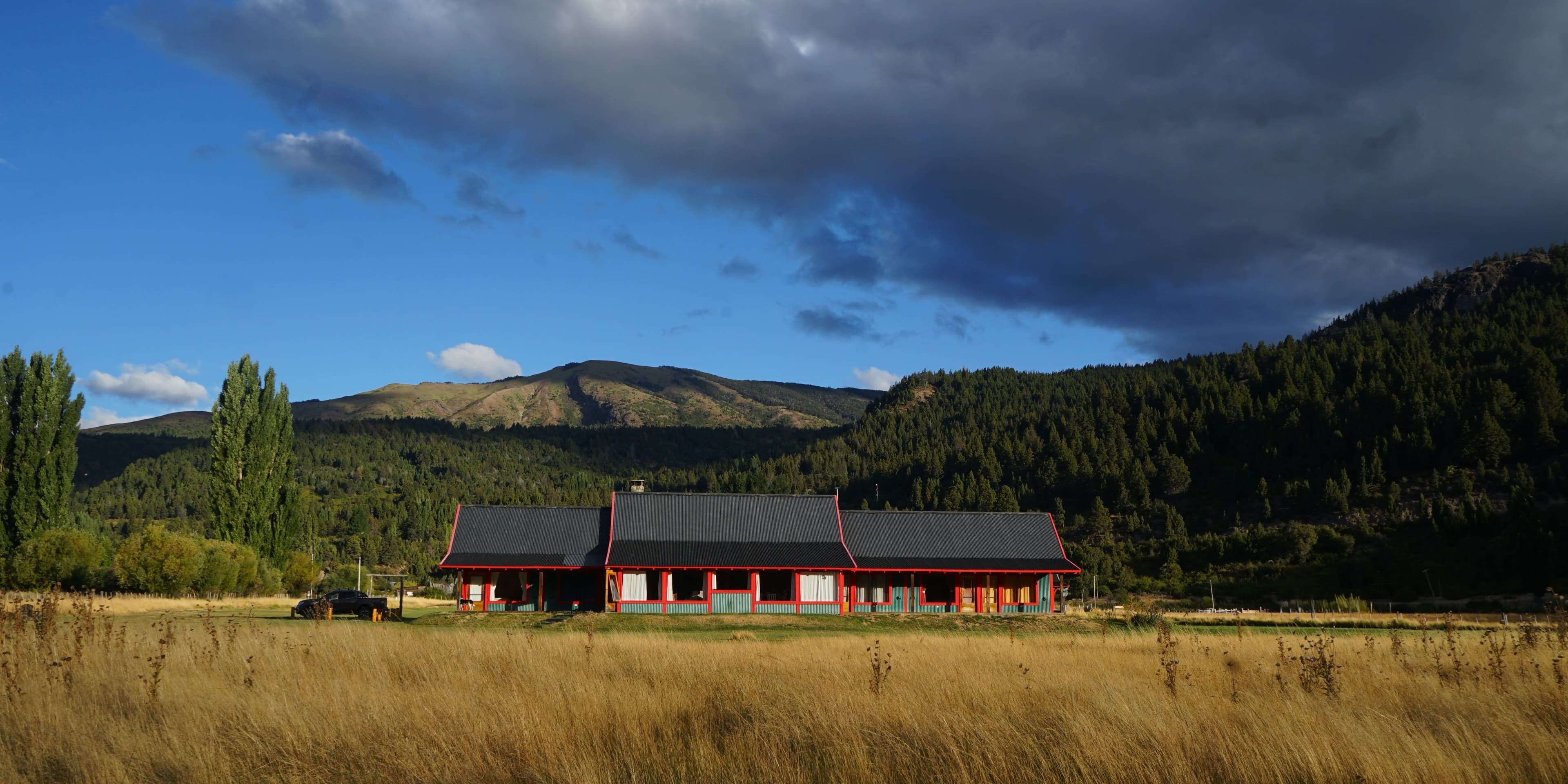 Instalaciones de La Pilarica Lodge junto a tres autos y montañas nevadas de fondo