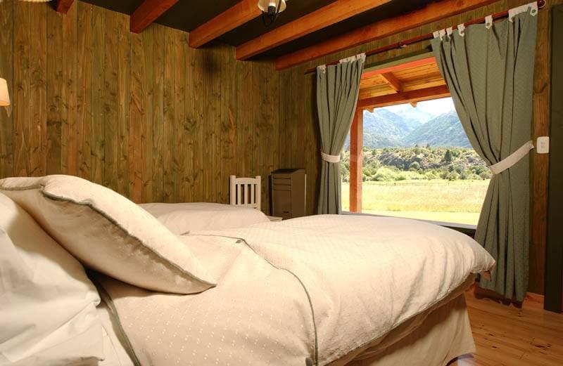 Facilities of La Pilarica Lodge with three cars and snowy mountains in the background