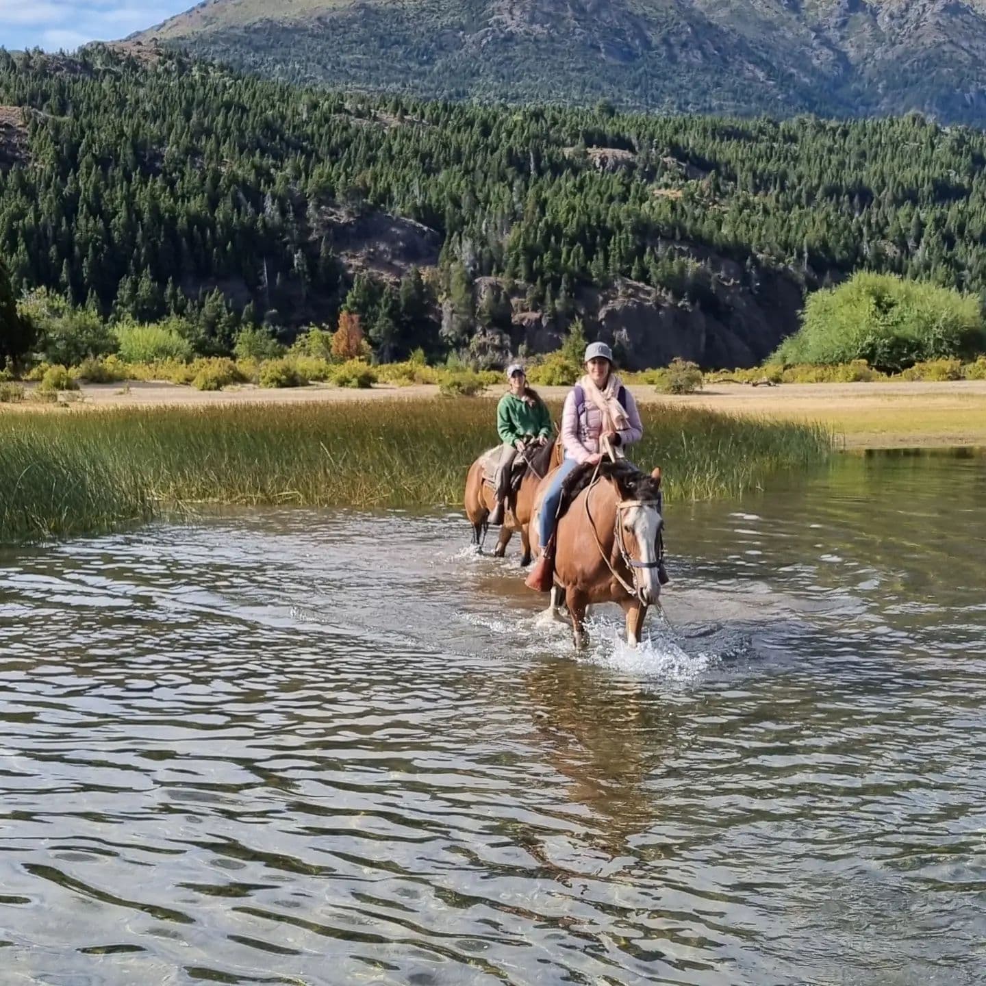 Two people riding horses crossing the river